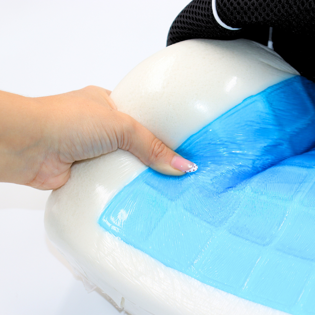 Dedo presionando el cojín lumbar y revelando la capa de gel refrescante azul bajo la espuma