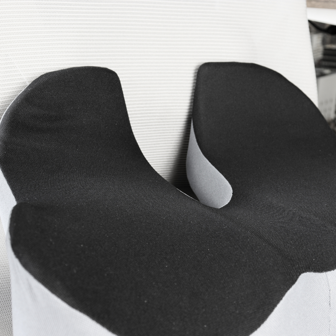 Cojín ergonómico con memory foam sobre silla de oficina, detalle del corte para el cóccix